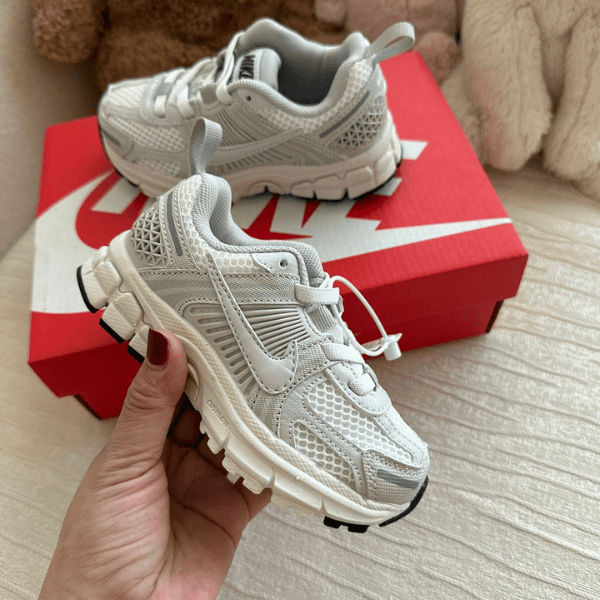 Pair of white sporty sneakers with chunky soles next to a red Nike shoebox, shown from a close-up angle for scale and detail.