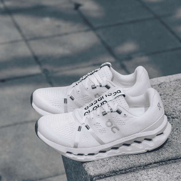 Pair of white athletic running shoes with chunky soles resting on a concrete step.