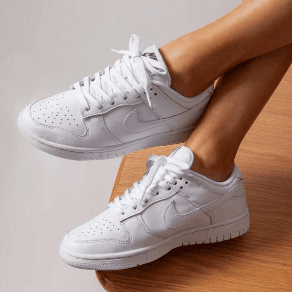 Pair of white sneakers on a person’s feet, resting on a wooden step, showing the Nike swoosh and laces.