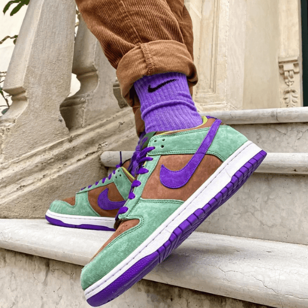 Colorful sneakers on stairs: green suede with purple Nike swoosh and purple accents, wearer in brown pants and purple socks.