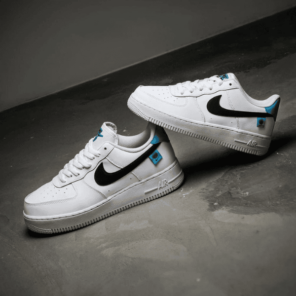 White Nike Air sneakers with a black swoosh and blue accents on a gray floor, photographed from a low angle.