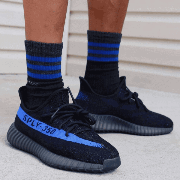 Close-up of black athletic sneakers with blue accents and 'SPLY-350' branding, worn with blue-striped socks on concrete ground.