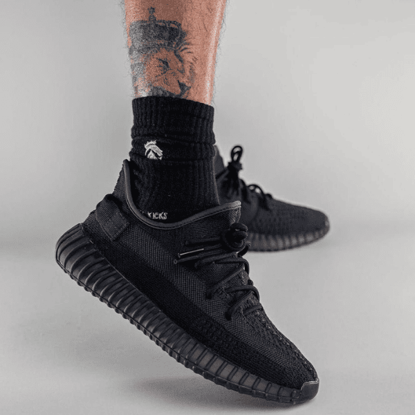 Close-up of a black knit sneaker on a foot, worn with a black sock, showcasing a ribbed, ridged outsole.