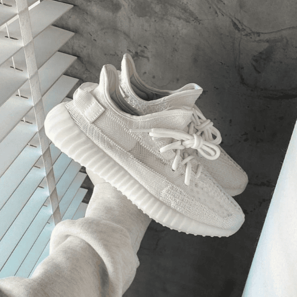 White knit sneakers with a chunky ridged sole held in a hand near window blinds