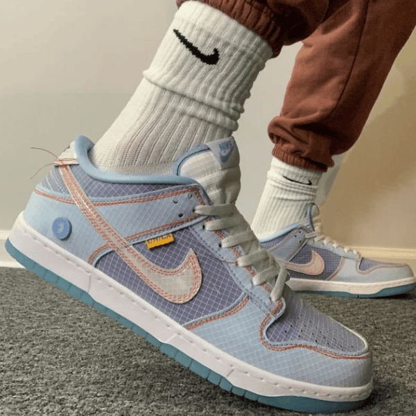 Person wearing light blue and pink Nike sneakers with white socks and a turquoise sole, standing on a carpeted floor