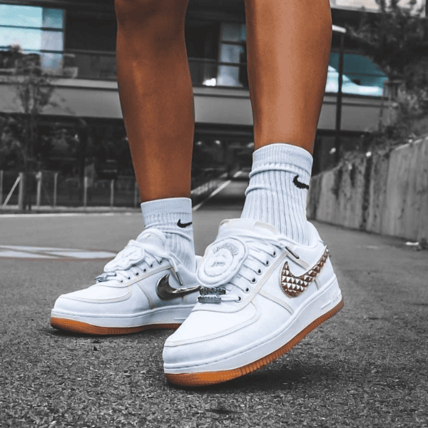Close-up of white Nike sneakers with gum soles on gray pavement, worn with light-blue ribbed socks.