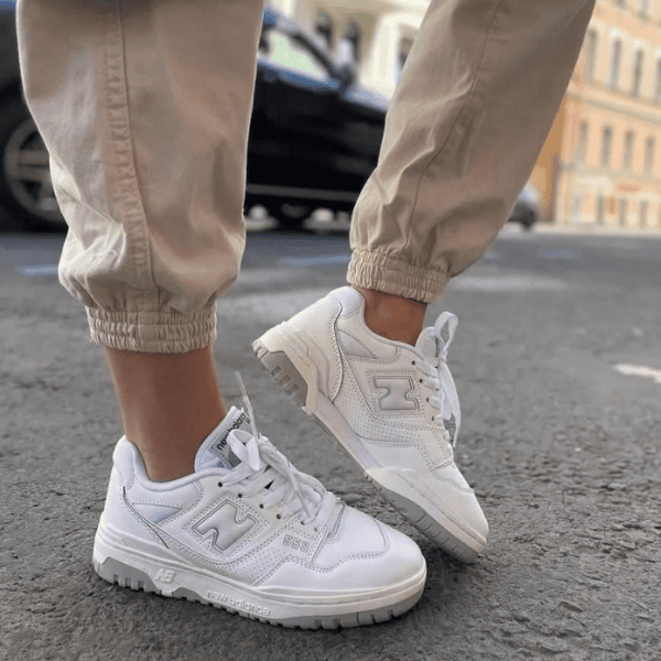 Person wearing white sneakers and beige jogger pants standing on a city street.