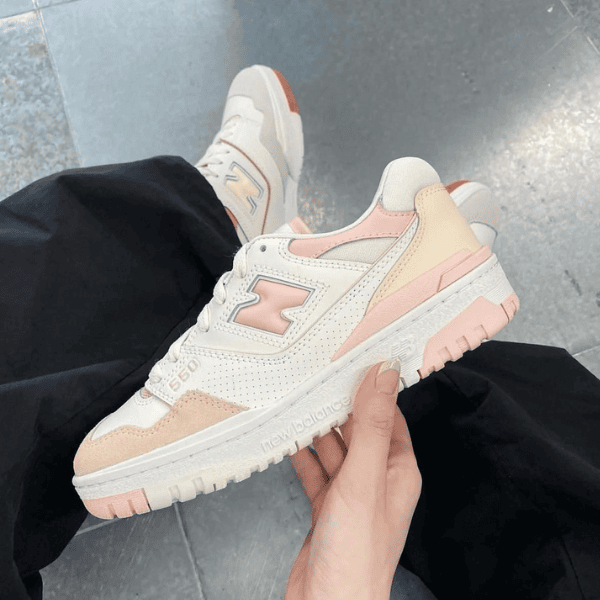 White and pastel pink New Balance sneaker held in hand, side view with N logo and perforated vamp image.