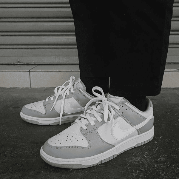 Close-up of gray and white Nike sneakers on a person standing on a dark pavement in front of a metal roll-up door.