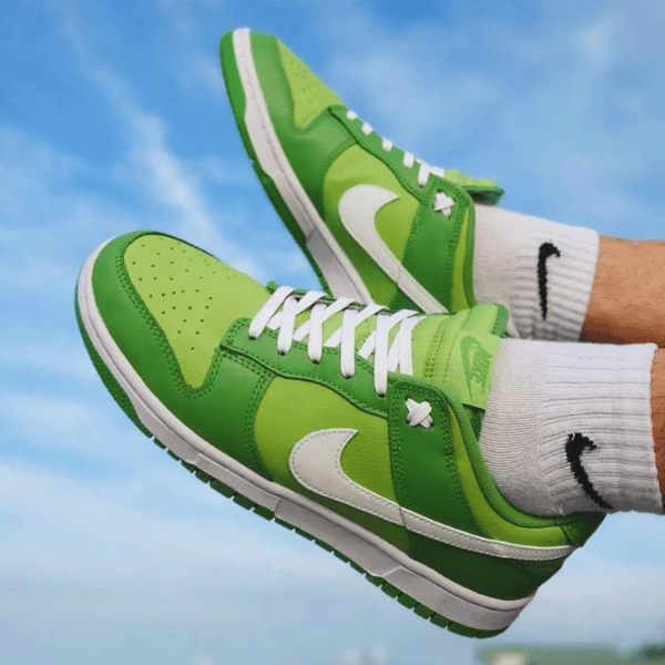 Pair of lime-green Nike sneakers with white swoosh and laces, worn with white socks against a blue sky.