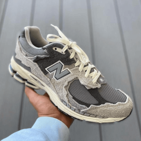 Gray New Balance running shoe with cream laces held in a hand, outer sole visible