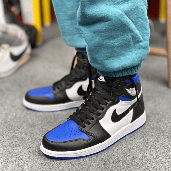 Close-up of blue, black, and white high-top sneakers on a gray floor, with teal joggers visible at the ankles.