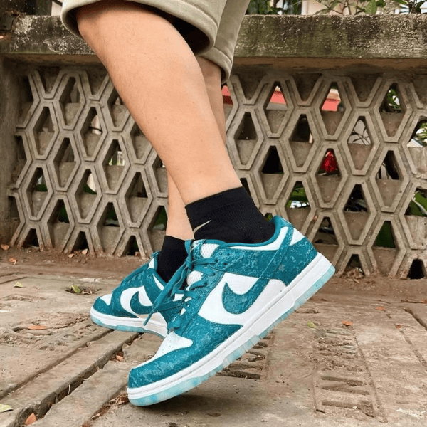 Feet in teal and white Nike sneakers on a concrete path, black socks, with a hexagonal lattice wall in the background.