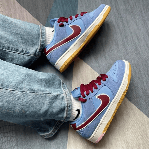 Blue sneakers with maroon Nike swooshes, white midsole and gum outsole, worn with jeans.