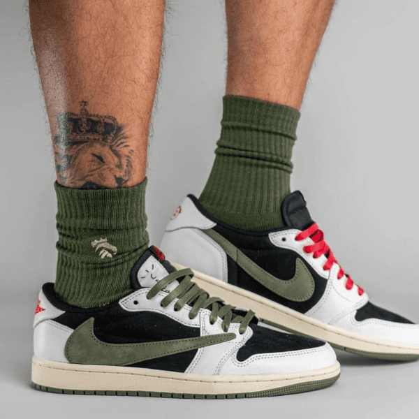 Pair of white, black, and olive sneakers with green laces and red accents, worn with olive socks, shown from the ankles down.