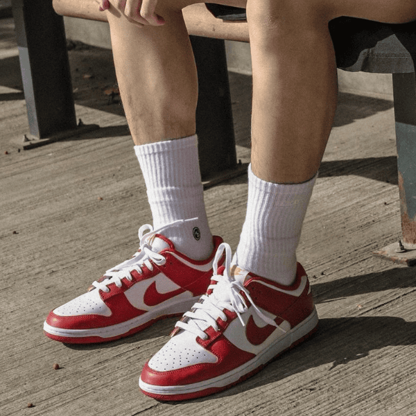 Red and white Nike sneakers worn with white crew socks, shoes resting on a concrete outdoor surface beside a bench.