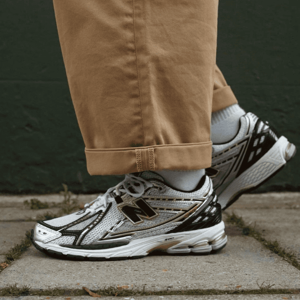 Close-up of someone wearing gray and black New Balance running shoes with tan cuffed pants standing on a concrete sidewalk.