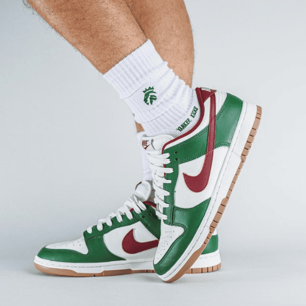 White and green high-top sneakers with a red swoosh, laces tied, and a gum sole on white socks.