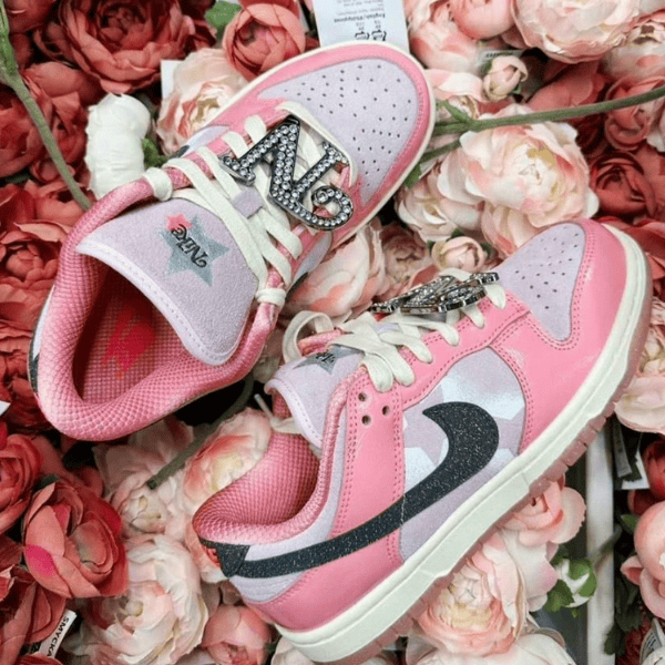 Pink children's sneakers with glittery '23' accents on the strap, set among pink roses.