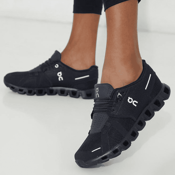 Person wearing black On running sneakers with a distinctive segmented hollow sole on a light floor surface