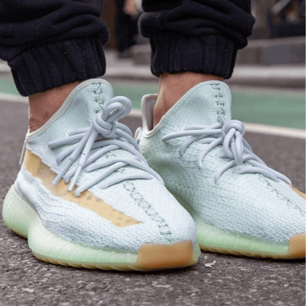 Close-up of mint-green athletic sneakers with light blue laces on a person standing on a paved street.