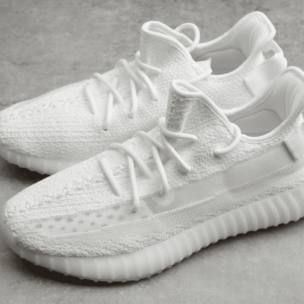Pair of white knitted sneakers with chunky ribbed soles on a gray surface.
