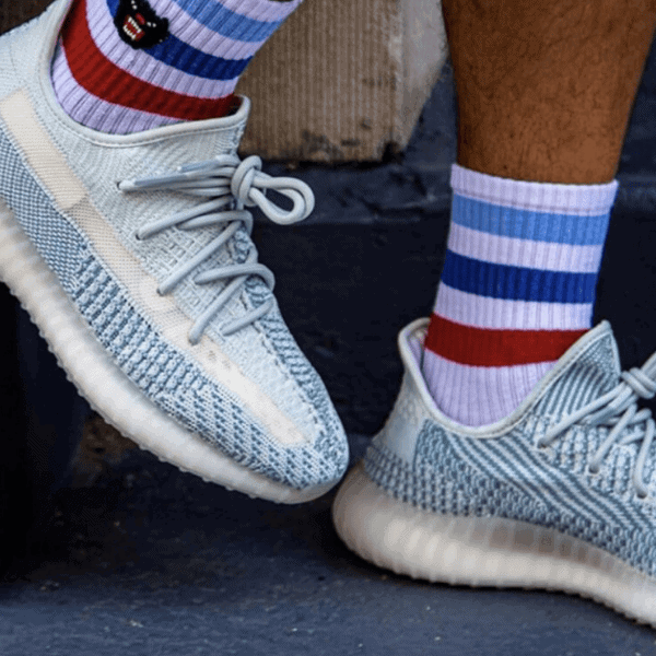 Light blue knit sneakers with pale laces on a dark stair, paired with red, white, and blue striped socks.