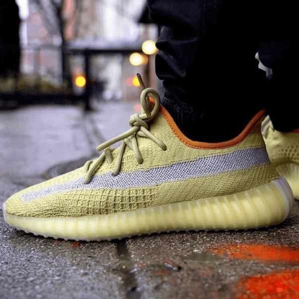 Close-up of a yellow knit sneaker with laces tied, resting on a wet city sidewalk edge.
