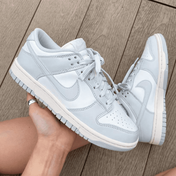 Light blue Nike sneakers with white overlays being held by a hand against a wooden deck background.