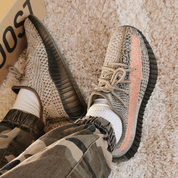 Person wearing beige and gray knit sneakers with white socks, camo pants, resting feet on a beige carpet.