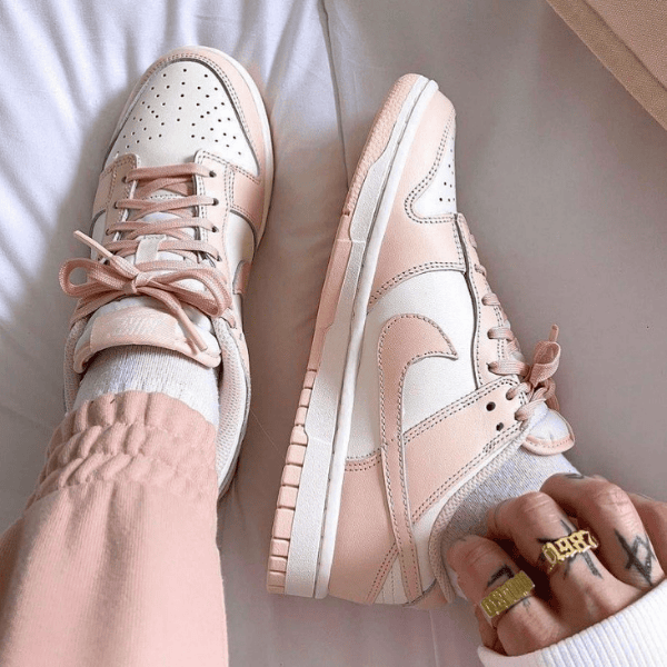 Pastel pink and white sneakers with laces on a person’s feet, wearing light pink pants