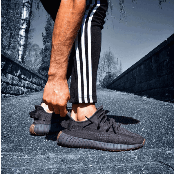 Person in black athletic shoes with striped track pants bending down to tie the laces on a paved path.