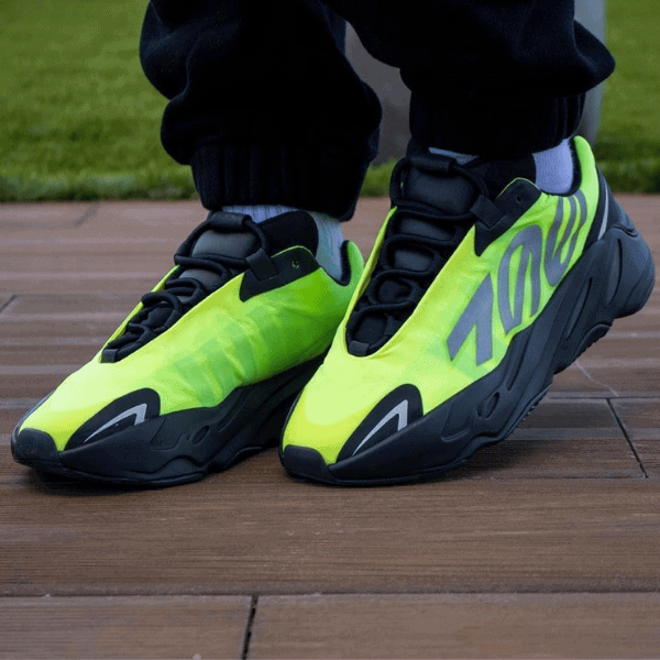 Pair of neon yellow-green athletic sneakers with black soles and laces resting on a wooden deck.