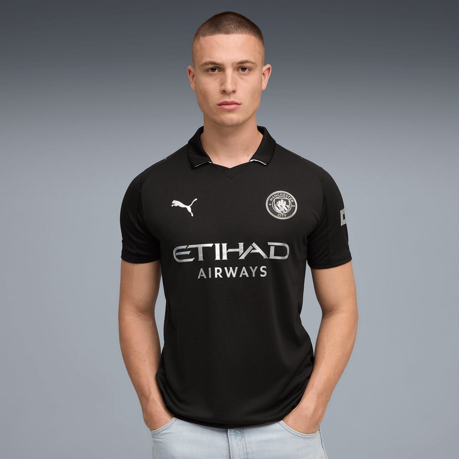 V6 | AE JERSEY Man wearing a black Manchester City football jersey with Etihad Airways sponsor, standing against a gray gradient background.