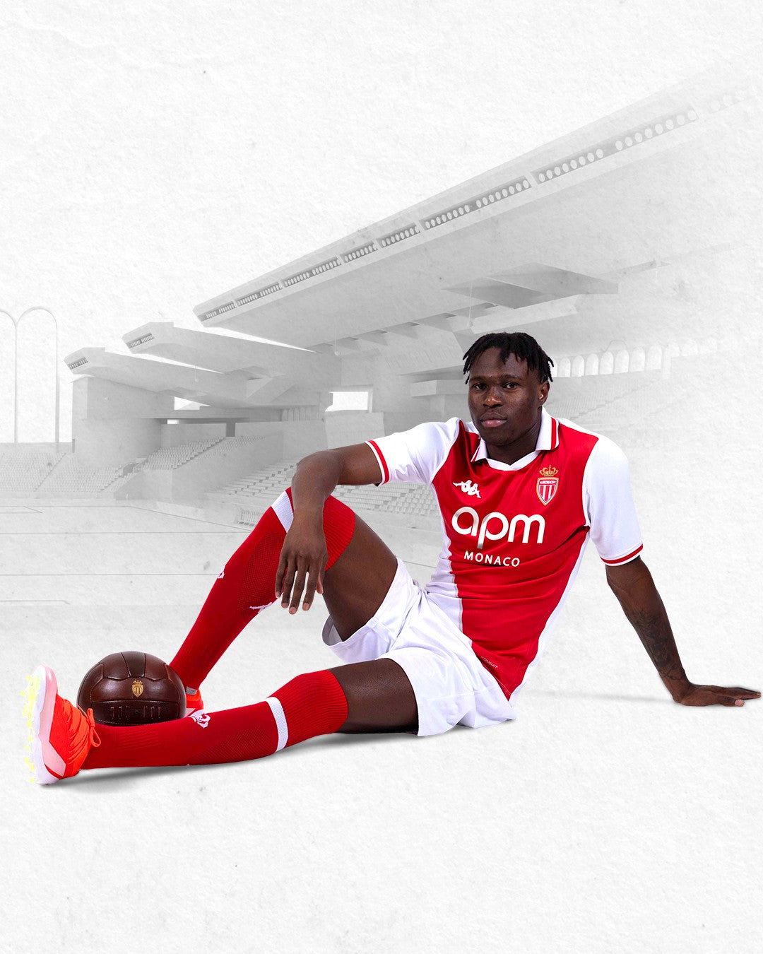 VCEVG3Rjd29lpDZ | AE JERSEY Footballer in AS Monaco kit sitting on the pitch with a brown football near his foot.