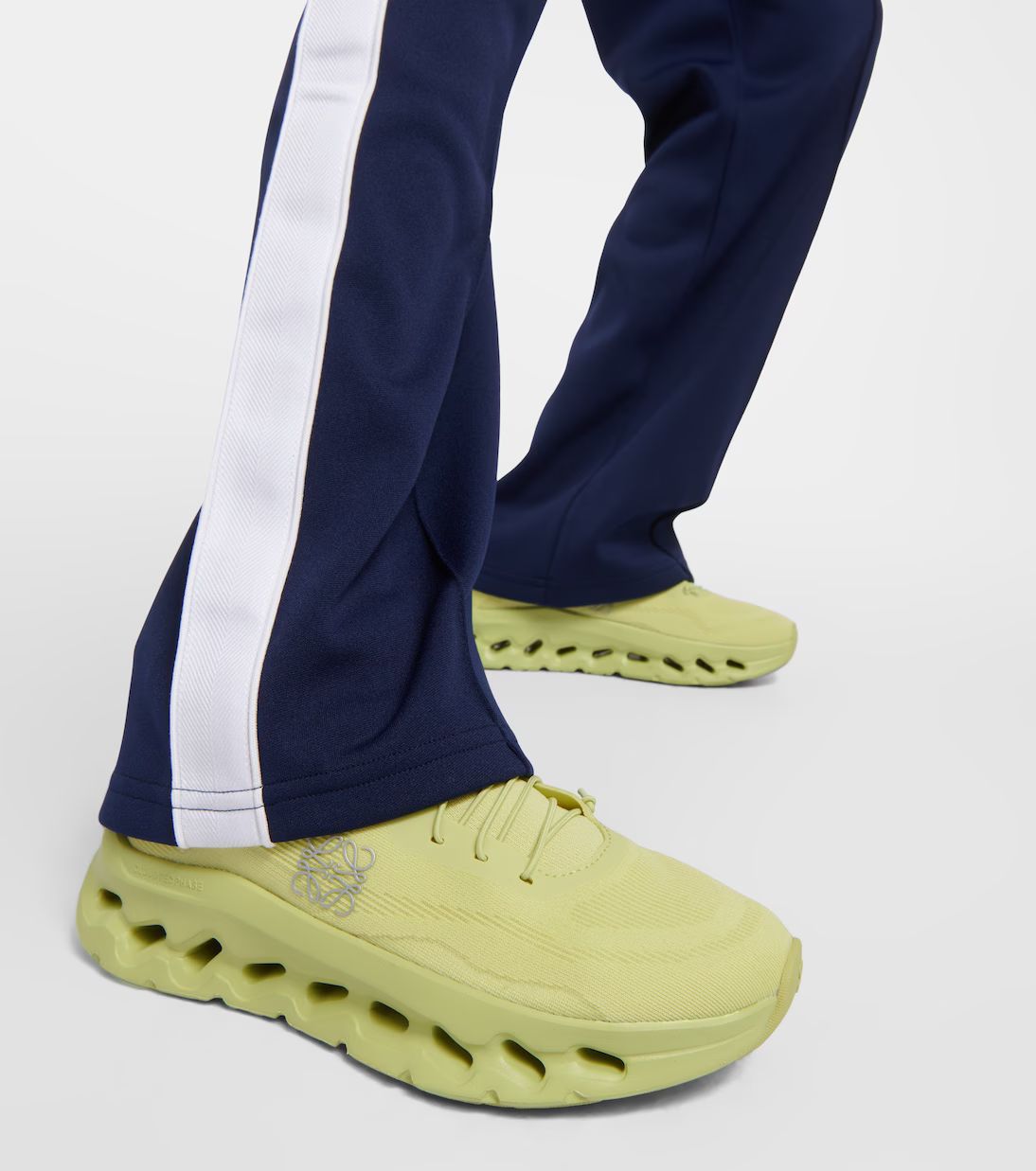 WhatsAppImage2024-07-22at18.36.42 | AE JERSEY Close-up of lime-yellow athletic shoes with chunky, perforated sole paired with navy track pants featuring a white side stripe on a white background.