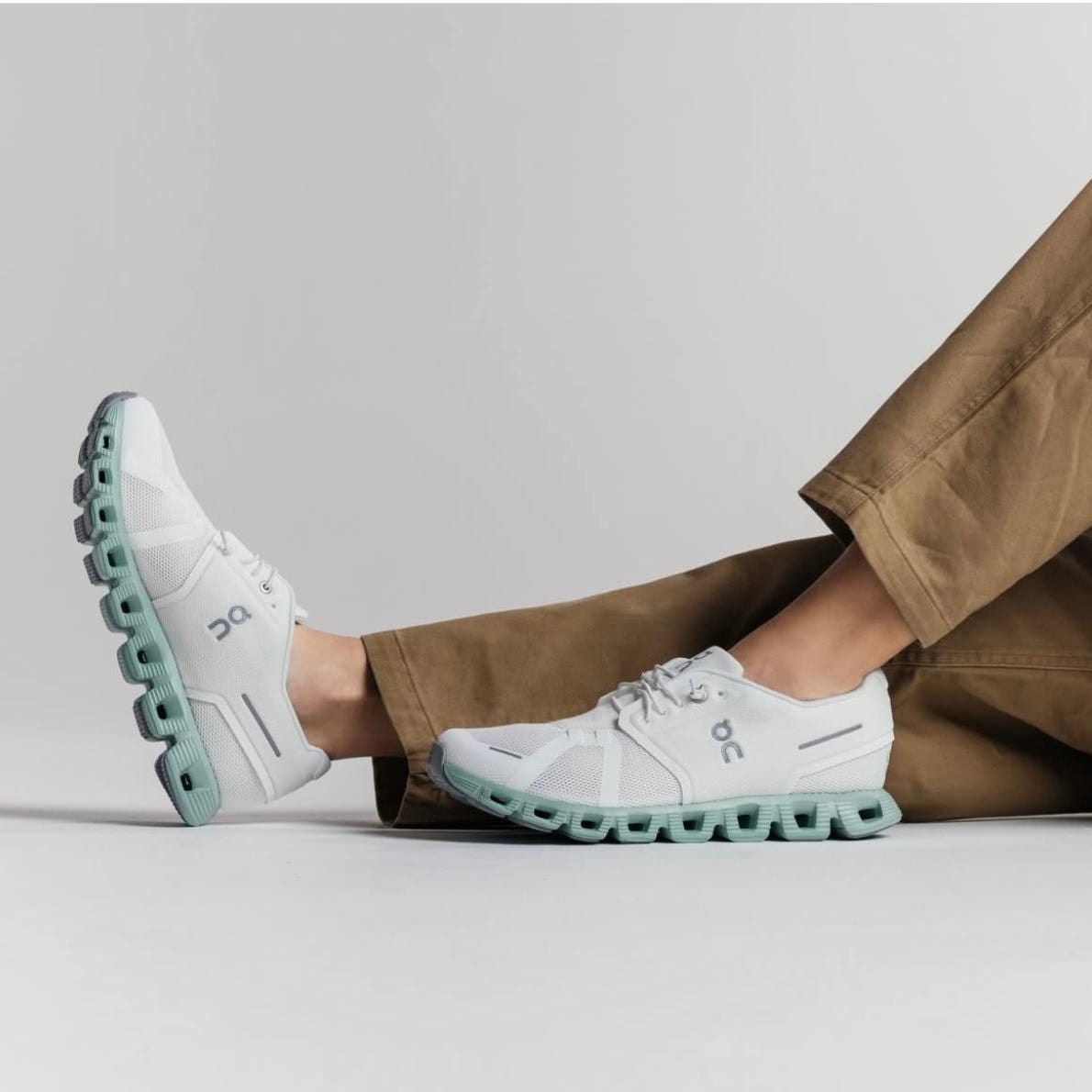 WhatsAppImage2025-01-26at09.34.25 | AE JERSEY White On running shoes with a mint-green, chunky sole shown in a side view with brown pants nearby.