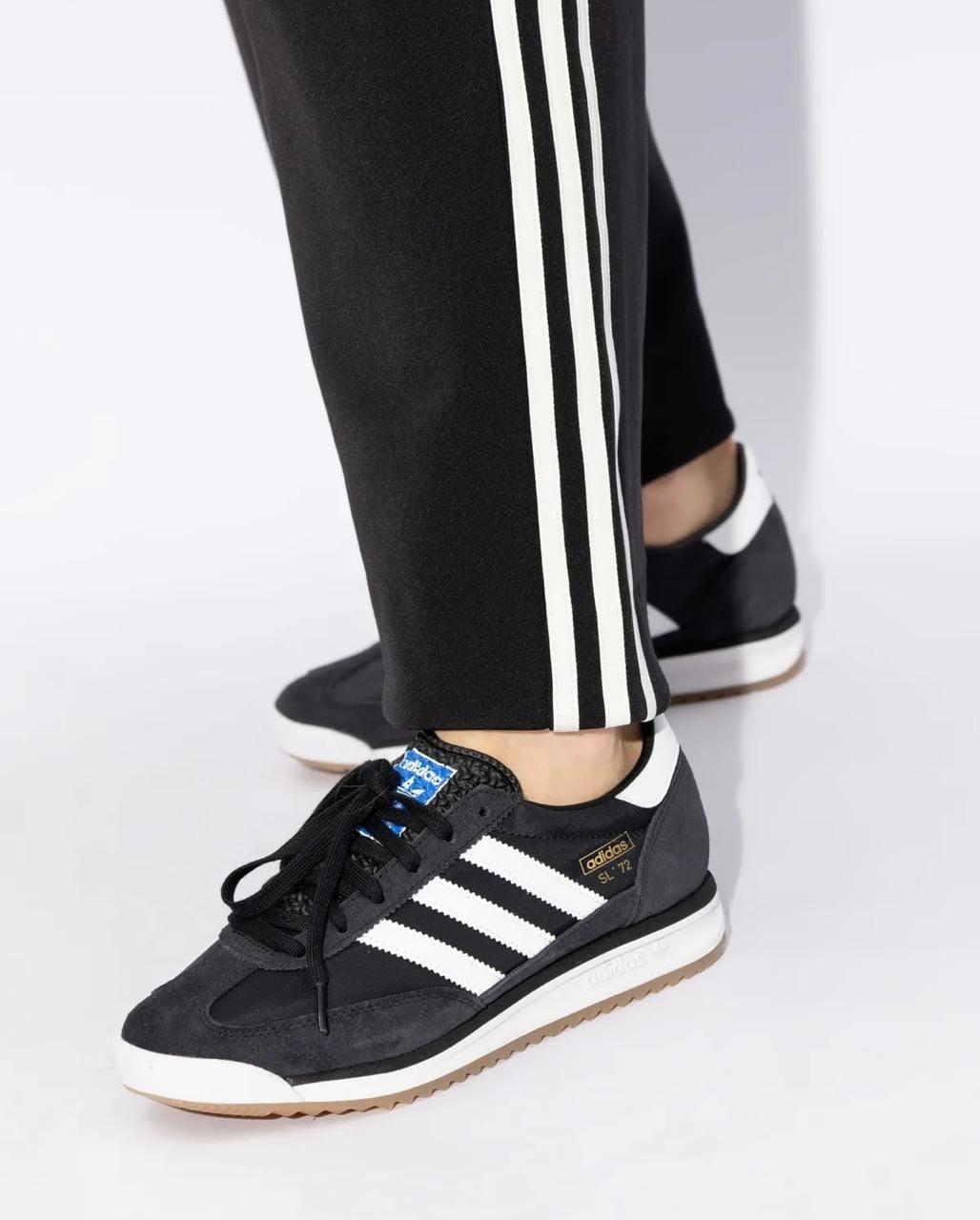 WhatsAppImage2025-04-15at11.26.53 | AE JERSEY Black Adidas sneakers with white stripes and laces, worn with black track pants featuring white side stripes.