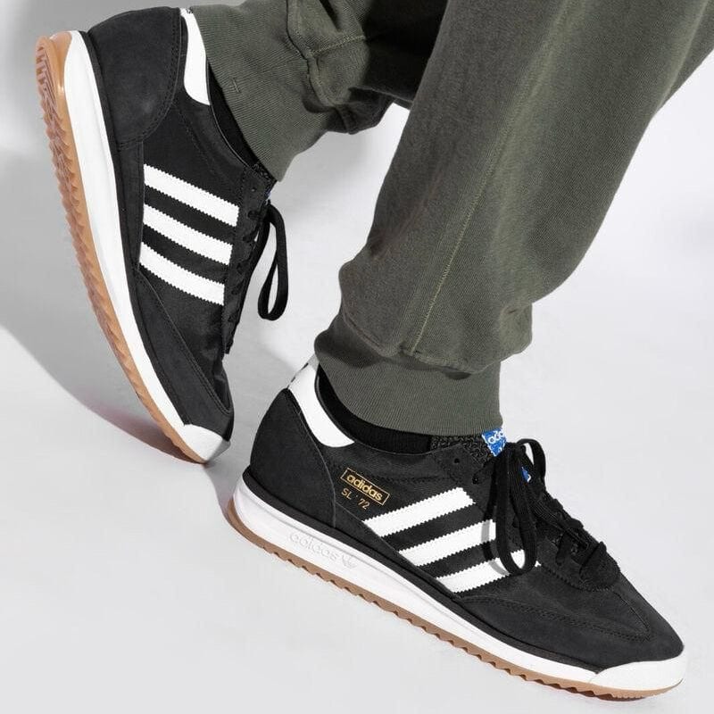 WhatsAppImage2025-04-15at11.27.03_2 | AE JERSEY Black Adidas sneakers with white stripes and gum sole, being worn by a person wearing olive-green pants