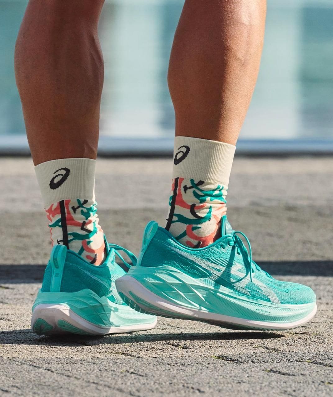 WhatsAppImage2025-05-12at12.39.02 | AE JERSEY Close-up of turquoise running shoes and patterned white socks standing on pavement.