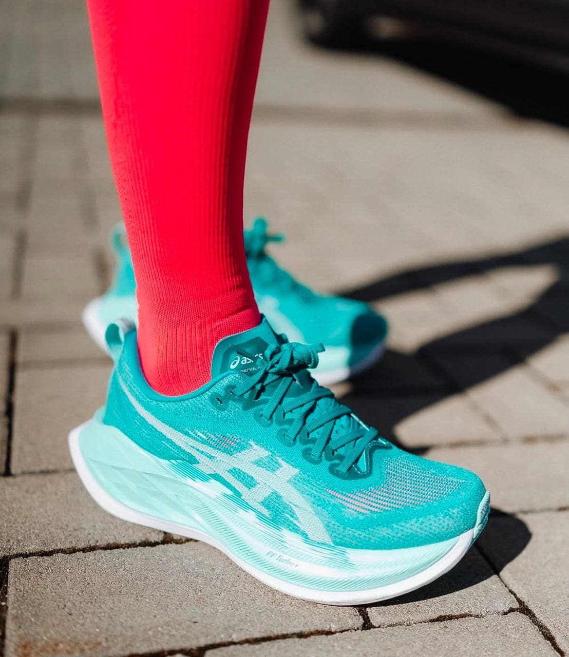 WhatsAppImage2025-05-12at12.39.15 | AE JERSEY Turquoise running shoes with bright pink socks on a paved sidewalk surface.