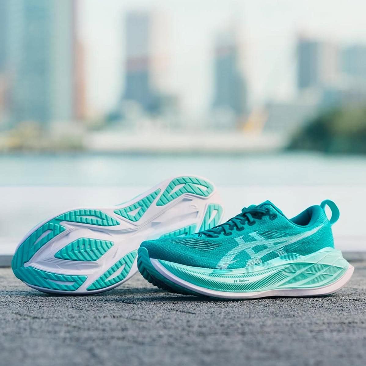 WhatsAppImage2025-05-12at12.39.26 | AE JERSEY Turquoise running shoes resting on a textured pavement with a blurred city skyline in the background.