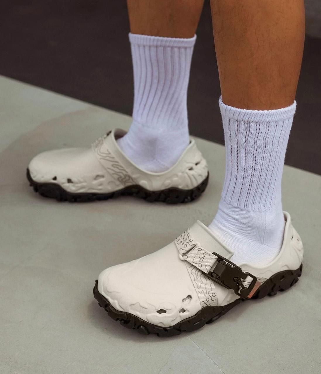 WhatsApp_Image_2024-09-07_at_11.22.30 | AE JERSEY Person wearing white open-toe sandals with a black rugged sole and white crew socks on a light floor edge of a room.