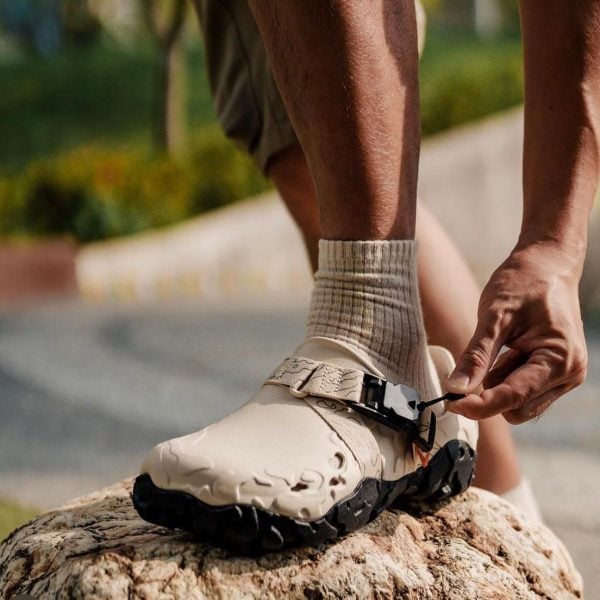 Close-up of a person tying the strap on a beige hiking boot while standing on a rock.