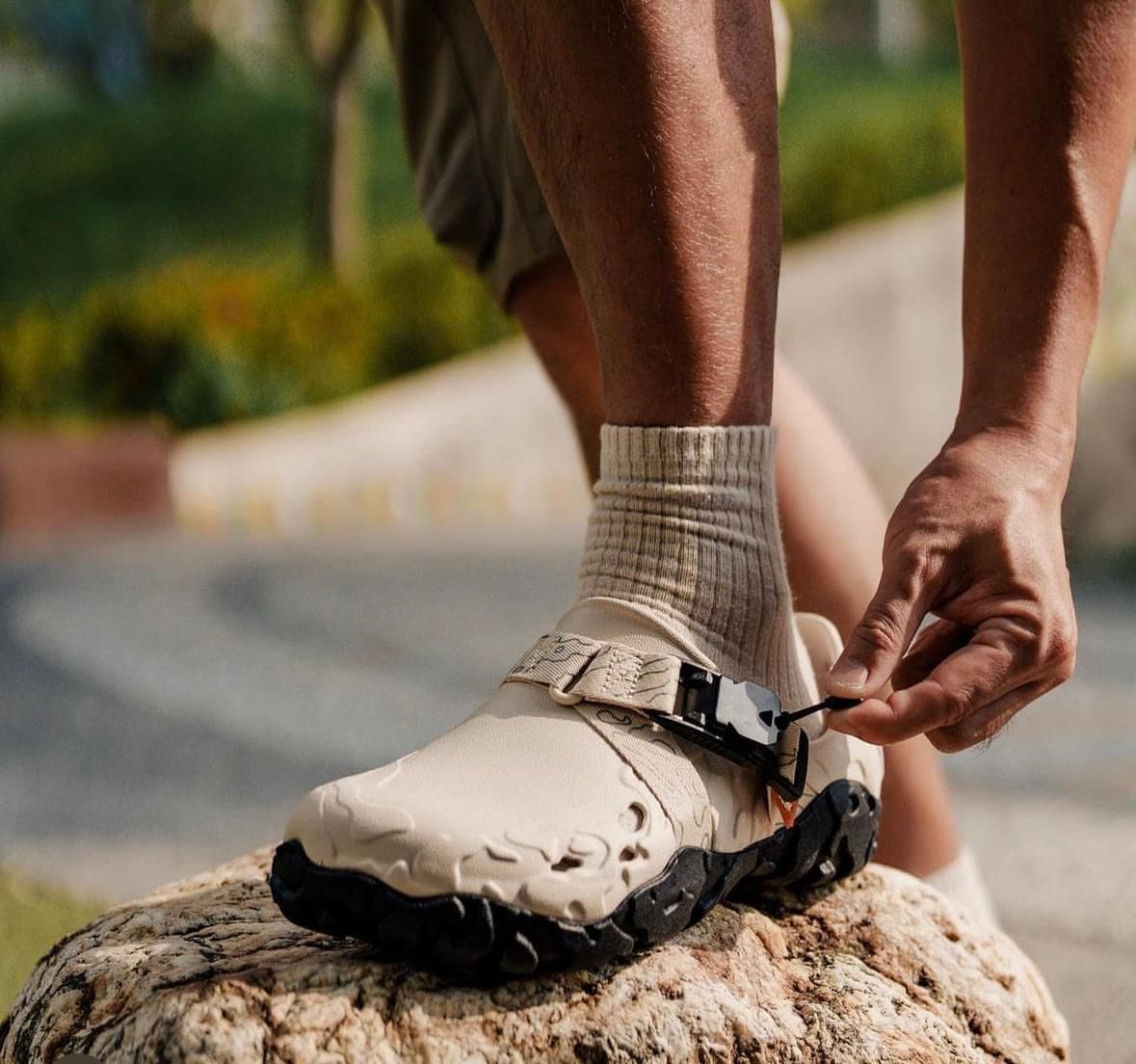 WhatsApp_Image_2024-09-07_at_11.22.32 | AE JERSEY Close-up of a person tying the strap on a beige hiking boot while standing on a rock.