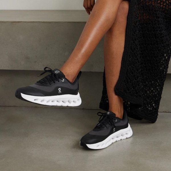 Woman wearing black sneakers with a chunky white sole, resting one foot on a step.