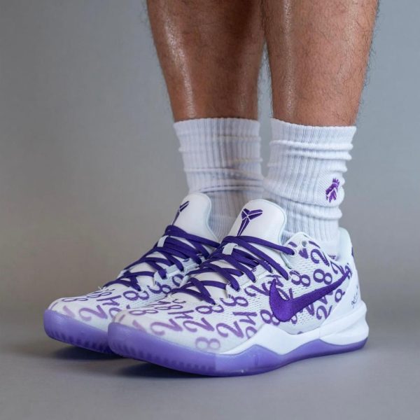 White and purple Nike basketball sneakers with a purple pattern and matching laces, worn with white crew socks.