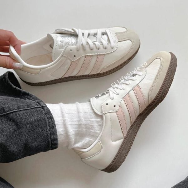 Pair of white sneakers with light pink side stripes, shown with white socks and jeans from a top-down angle (lifestyle photo).