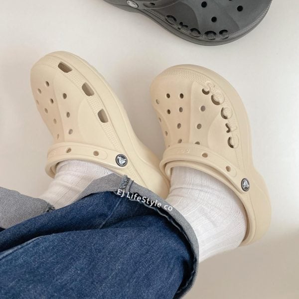 Beige Crocs-style clogs worn with white socks and cuffed jeans, photographed from above.