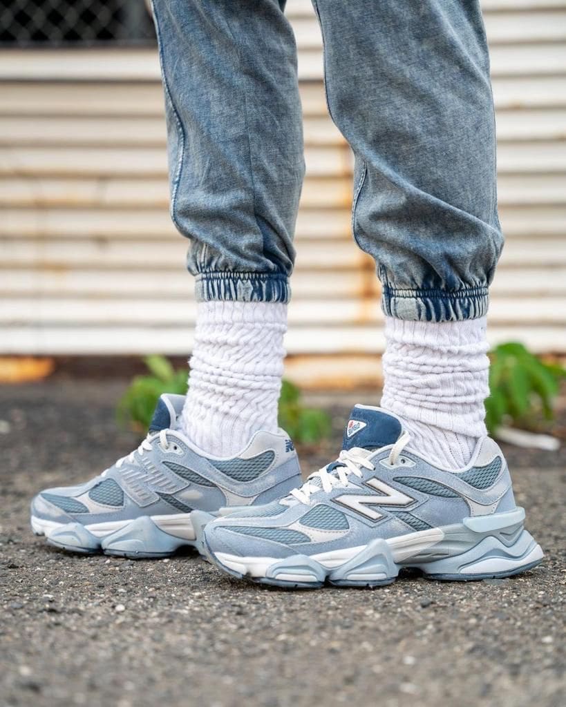 WhatsApp_Image_2024-10-26_at_16.18.01 | AE JERSEY Close-up of legs wearing light-wash jeans, thick white scrunched socks, and gray/blue athletic sneakers standing on asphalt.